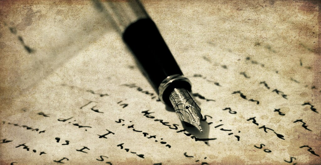 Closeup photo of a decoratively engraved fountain pen and an open journal page, covered with handwriting in black ink.
